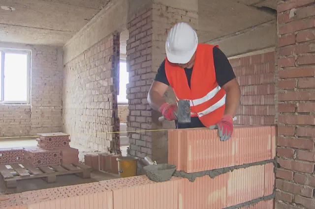A construction worker in a hard hat lays bricks inside an unfinished building